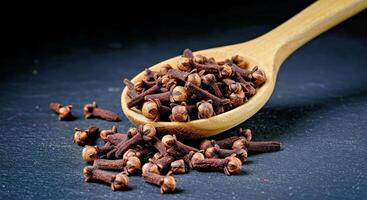 Clove Spice Spilling from a Rustic Wooden Spoon Against a Dark Background photo