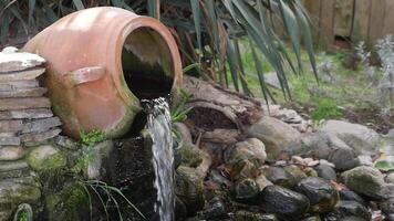 Water flowing from a clay pot into a tranquil garden setting video