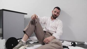 A businessman in a trashed office sits on the floor. Stress, chaos and business man with headache due to paperwork, reports. Concept of burnout video