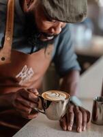 A warm and professional coffee shop scene featuring a barista in a brown apron and cap, carefully presenting a metallic cup of latte with elegant heart-shaped latte art. photo