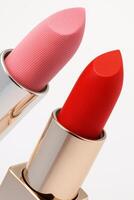 Macro close up of two luxurious lipsticks one soft pink and the other bold red with an elegant geometric texture on the surface, displayed in shiny golden cases. photo