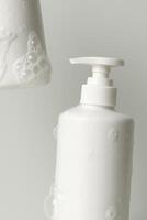 Minimalistic composition showing two white plastic pump bottles covered with rich, airy soap bubbles. The bottles are clean, simple in shape photo
