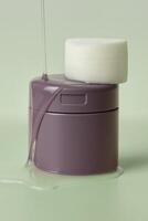 Close-up of a stack of white skincare toner pads placed on a glossy mauve jar, with clear serum flowing smoothly down the sides and pooling around the base. photo