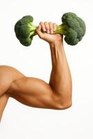 A muscular male arm holds a dumbbell made from two broccoli heads connected by a stalk. photo