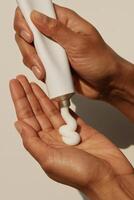 Close-up of two hands against a neutral background, one hand holding a white cosmetic tube and the other receiving a swirl of white cream. photo