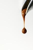 A hyper-realistic close-up macro image of a rich espresso drop hanging from a polished metal portafilter spout, just before falling. photo
