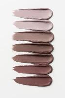 Minimalist flat-lay of seven creamy nude lipstick swatches in a vertical arrangement on a clean white background. photo