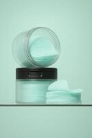 Minimalist close-up of two transparent jars filled with mint-colored skincare toner pads, placed on a glass surface with matching mint green background. photo