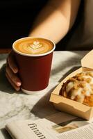 A cozy coffee break scene with a hand holding a red paper cup filled with latte featuring elegant leaf latte art on top. photo