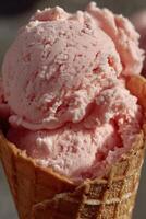 Close-up of a creamy pink strawberry ice cream served in a crispy waffle cone. The texture is soft and slightly fluffy, with scoops piled generously and catching bright daylight. photo