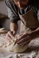 A close-up view of a bakers floured hands gently shaping a round piece of bread dough on a surface dusted with flour. photo