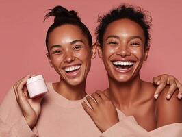 Two smiling young women with natural, makeup-free skin pose against a soft pink background. One holds a white cosmetic jar, while the other gently touches her shoulder. photo