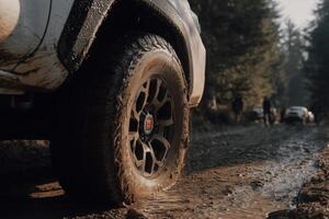 A close-up of a rugged TRD off-road tire partially covered in mud, gripping a wet forest trail. photo