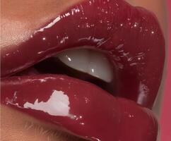 Extreme close-up of lips with deep burgundy glossy lipstick, reflecting soft studio light. photo