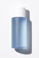 Minimalist product shot of a blue frosted glass skincare bottle with a solid white cap, centered against a pure white background. photo