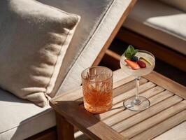 Top-down view of two elegant summer cocktails placed on a light wooden table in an outdoor lounge setting. photo