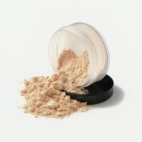 Minimalist beauty flat-lay showing a transparent round jar of beige loose setting powder, tipped over with powder spilling naturally onto a clean white surface. photo