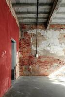 A raw, industrial loft-style interior featuring exposed red brick walls with patches of worn plaster, a concrete floor, and a rough ceiling photo