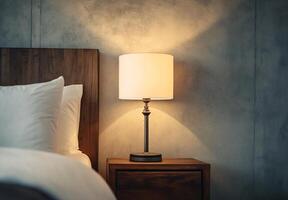 A lamp is on a wooden nightstand next to a bed photo