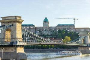 Chain Bridge over Danube River with Buda Castle in the background and tourist boat passing in Budapest, Hungary photo