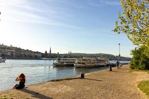 Scenic riverside view of Danube in Budapest with docked cruise boats, historic cityscape in background, and people relaxing on the promenade photo