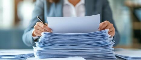 A person reviewing documents amidst a large stack of papers in a professional setting. photo