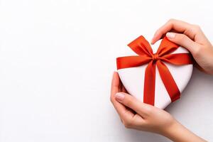 Gift box held with hands, adorned with a red ribbon on a light background. photo