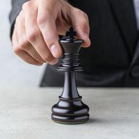 A hand placing a black king chess piece on a table. photo