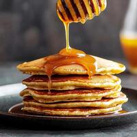 Stack of pancakes drizzled with honey on a dark plate. photo