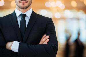Confident man in suit with arms crossed in a blurred background setting. photo