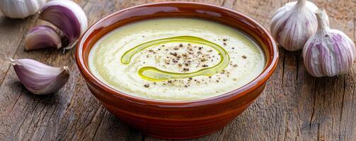 Creamy garlic sauce in a bowl with fresh garlic cloves nearby. photo