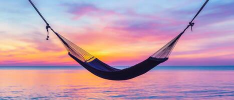 Hammock over tranquil waters at sunset with colorful sky. photo