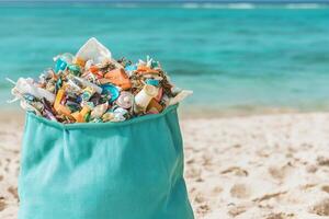 Bag of plastic waste on a beach with turquoise ocean in the background. photo