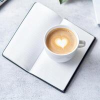 Coffee cup with heart design on an open notebook. photo