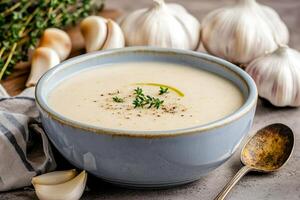 Creamy garlic soup with herbs in a blue bowl and garlic cloves nearby. photo