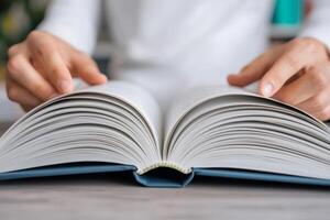 Open book with hands turning the pages on a wooden surface. photo