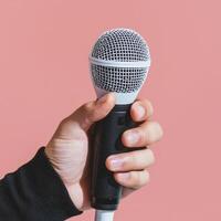 Hand holding a microphone against a pink background. photo