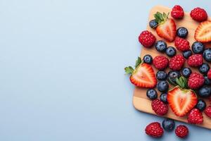 Fresh berries arranged on a wooden board against a light blue background. photo