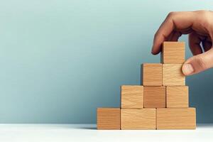 Hand stacking wooden blocks on a table against a light background. photo