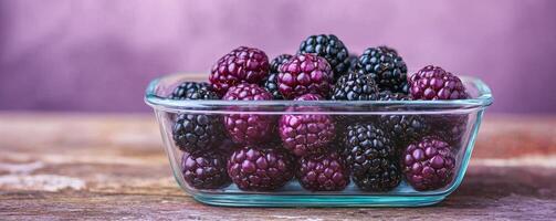 Fresh blackberries in a glass bowl with a soft purple background. photo