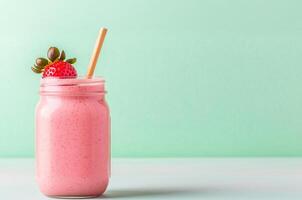 Smooth pink smoothie in a jar with a straw and strawberry garnish. photo