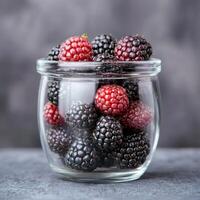 Glass jar filled with blackberries and raspberries on a gray surface. photo