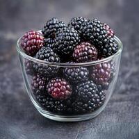 Fresh blackberries in a clear glass bowl against a dark background. photo