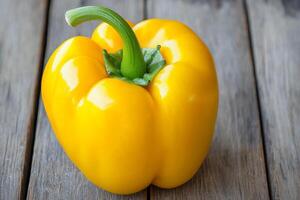 Bright yellow bell pepper on wooden surface. photo