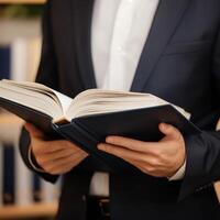A person in a suit reading a book with focused interest. photo