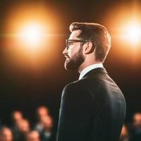 Man in suit speaks to audience under bright lights. photo