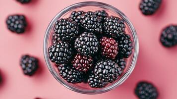 Fresh blackberries in a glass bowl on a pink background photo