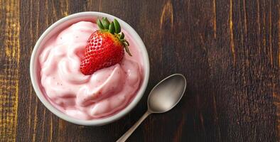 Creamy strawberry yogurt in a bowl with a spoon on wooden background. photo