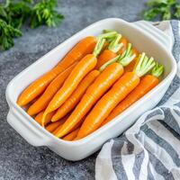 Fresh carrots arranged neatly in a white dish on a textured background. photo