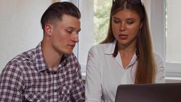 Two business colleagues smiling at the camera while collaborating on a laptop video